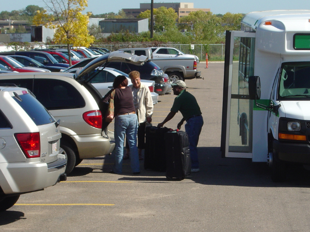 People loading luggage into a car at offsite airport parking lot.